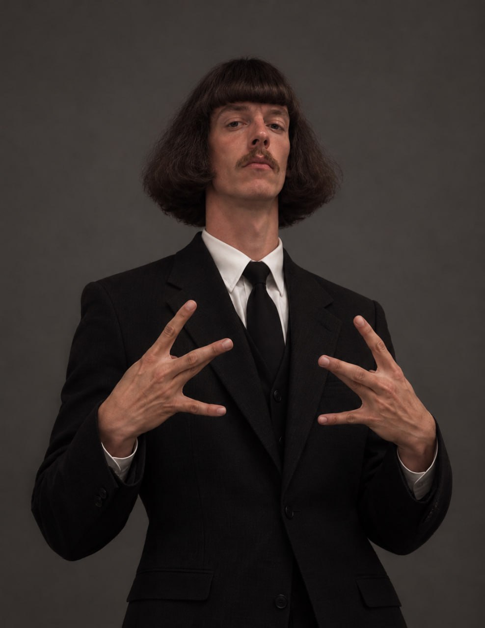 SOL Phil holds his hands up in a framing gesture, wearing a black suit